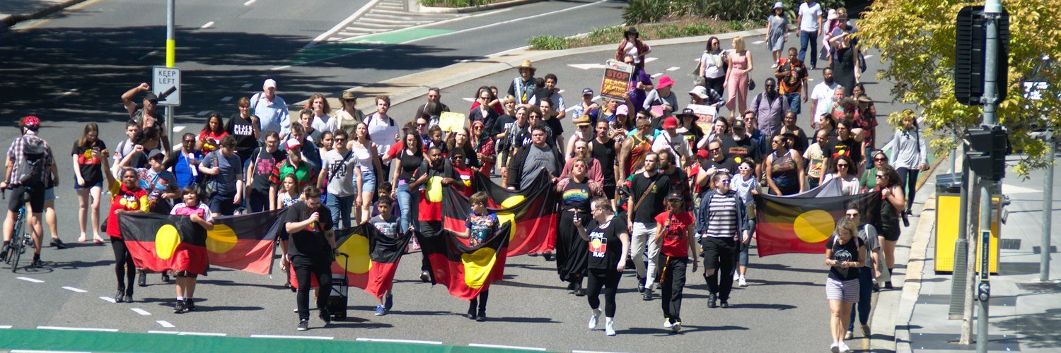 Marchers led by young people carry six Aboriginal flags along a Brisbane street towards Queensland Police headquarters