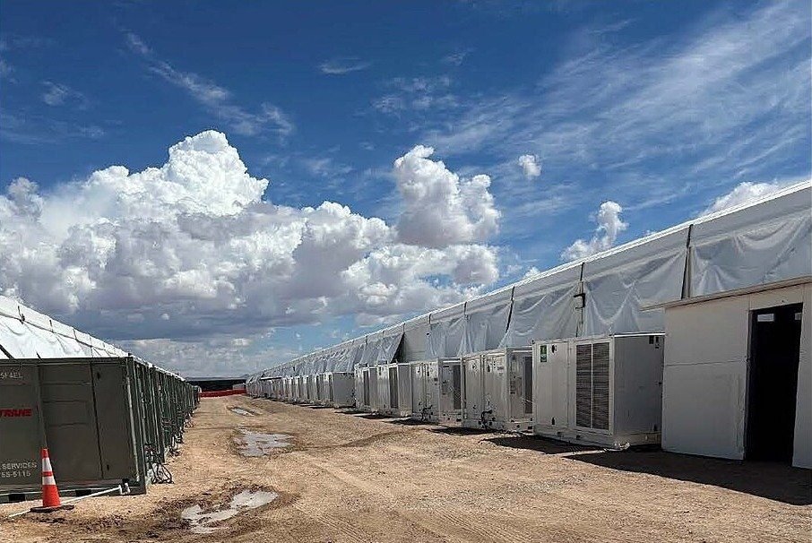 Long rows of white tent buildings with air-conditioning units on bare dirt under a blue sky