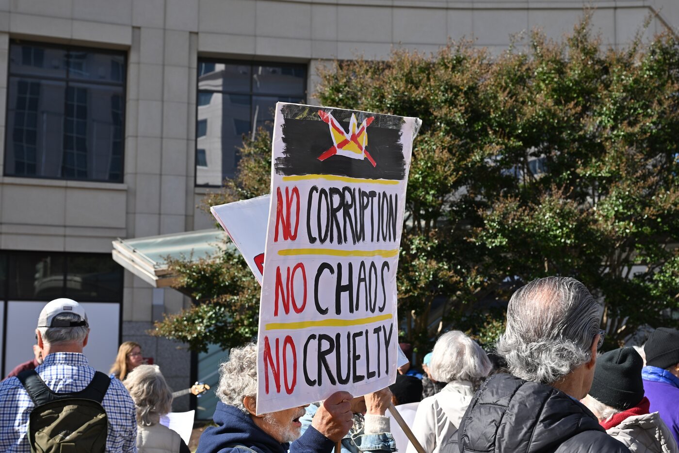 A protester holds up a hand-lettered sign reading No Corruption, No Chaos, No Cruelty beneath a crossed-out crown