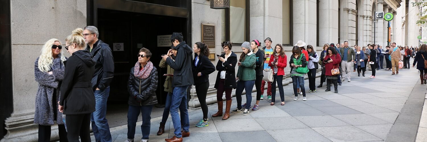 A long line of voters in coats stretches along the stone front of a city office building and down the sidewalk