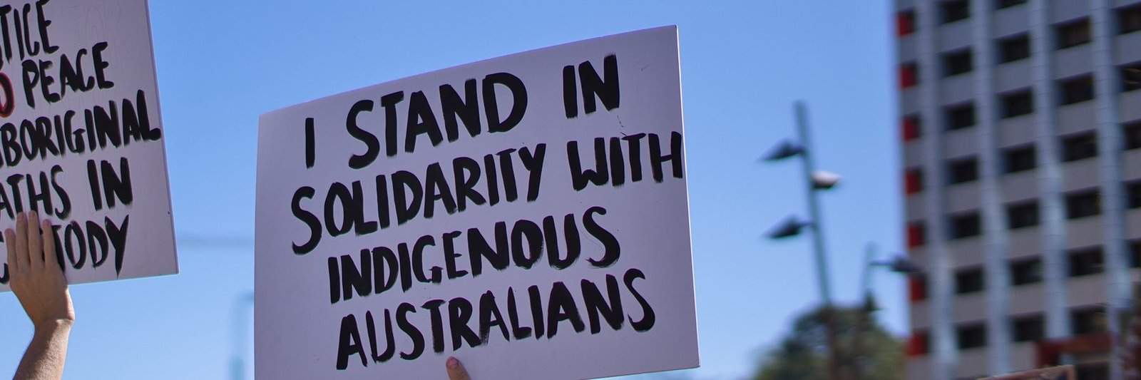Placards held up at a Brisbane rally; one reads I stand in solidarity with Indigenous Australians, and another, Justice and peace, Aboriginal deaths in custody