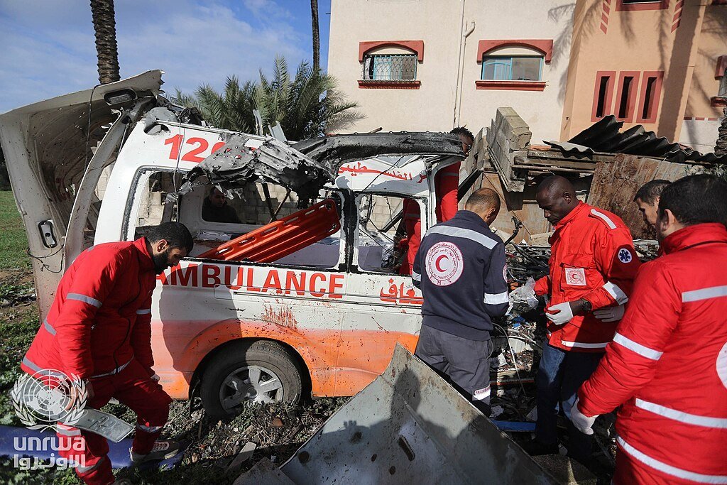 Palestine Red Crescent personnel inspecting a destroyed ambulance beside a building