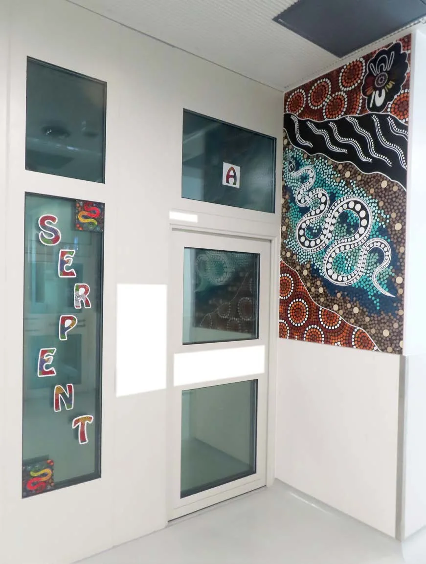 A dot-painted serpent mural in ochre, black, and blue beside the glass door of an accommodation pod lettered Serpent